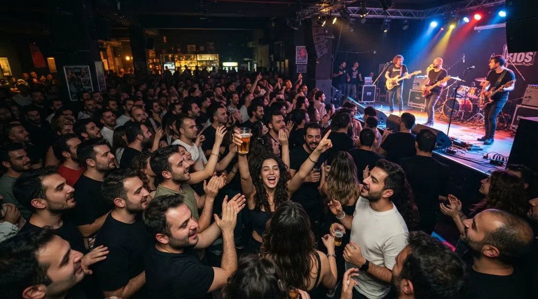 una noche concurrida en Bios en Kıbrıs Şehitleri Caddesi, gran escenario en vivo iluminado, público abarrotado, energía de concierto y vasos levantados en una sala oscura