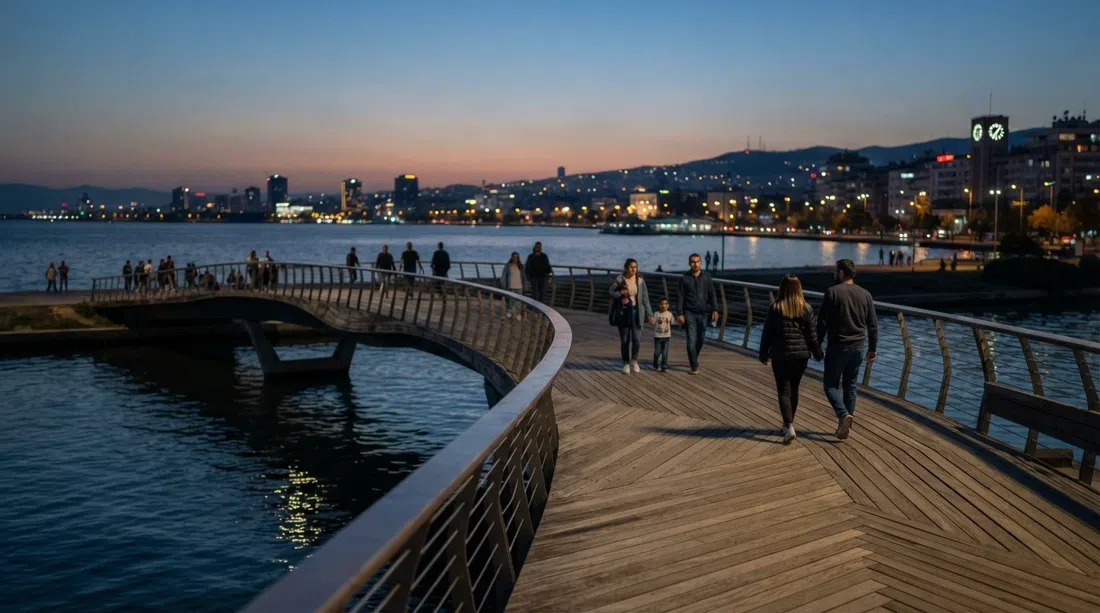 Bostanlı Footbridge sobre el arroyo al atardecer, tablas de fresno anguladas y vistas abiertas de la bahía con la ciudad al fondo